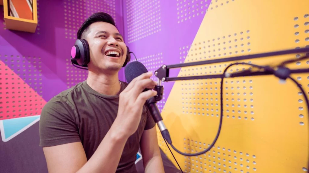 Young man talking into a mic with headphones on smiling