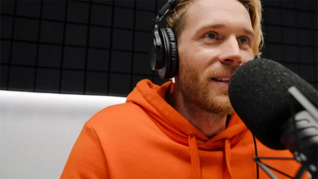 Podcaster with orange hoodie on talking into microphone