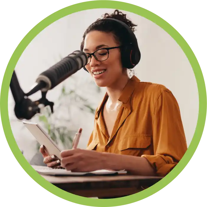 Woman with mic and headphones wearing glasses and holding a tablet and paper to illustrate the ease of podcasting with a good podcast host.